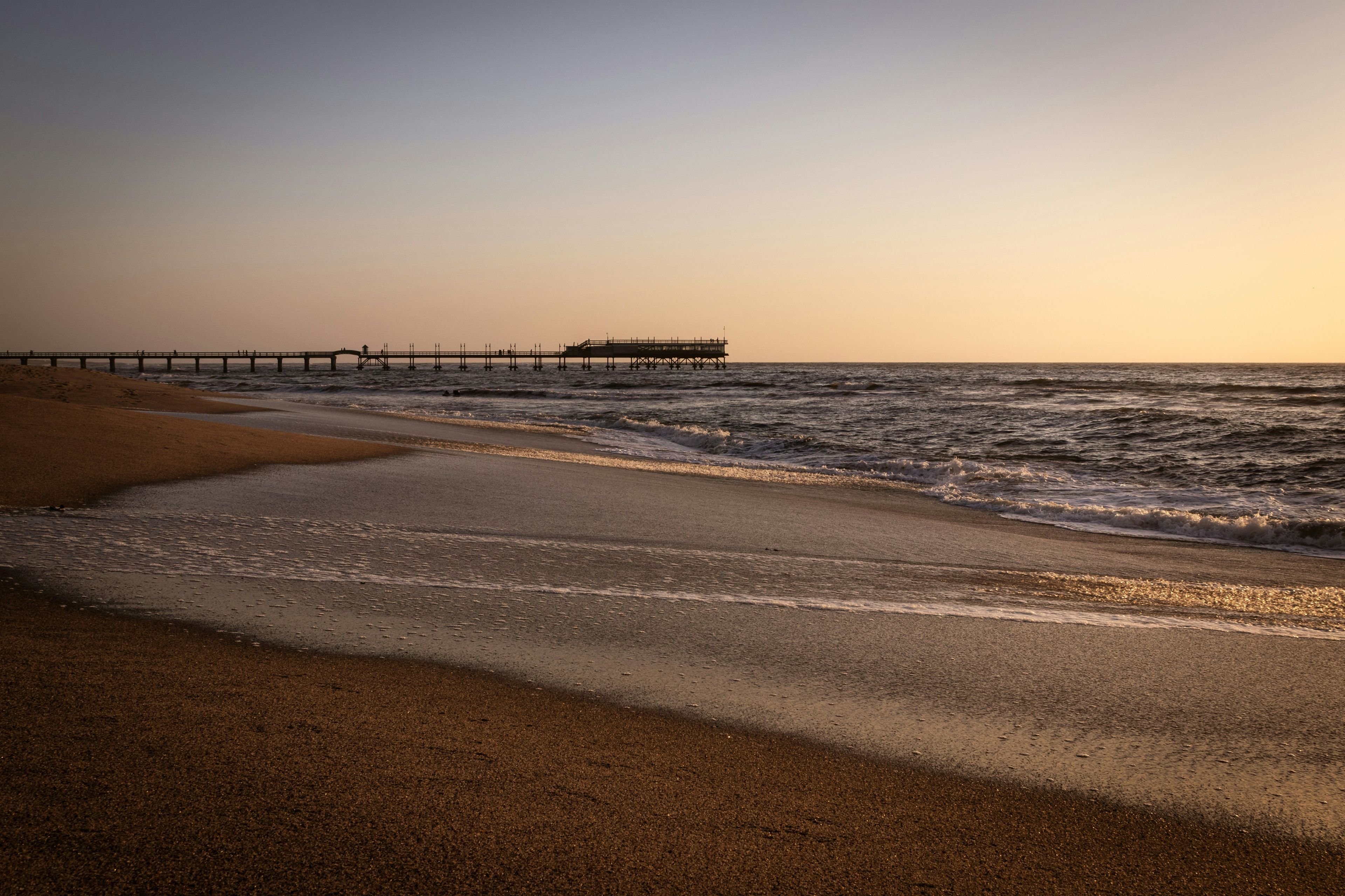 Newport Beach coastline with golden sand, blue waves, and the iconic pier at sunset